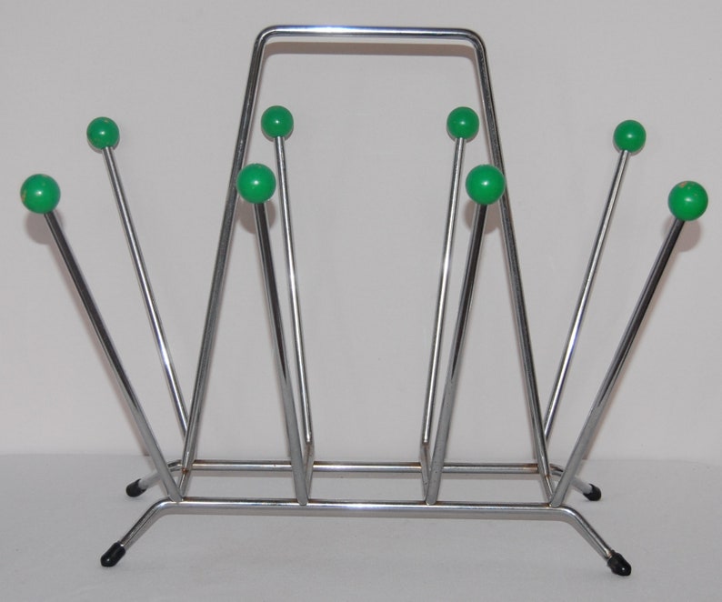 Peut inclure: Un porte-revues en chrome avec un design g&eacute;om&eacute;trique et des accents de boules en plastique vert. Le porte-revues a une base rectangulaire et un cadre triangulaire.