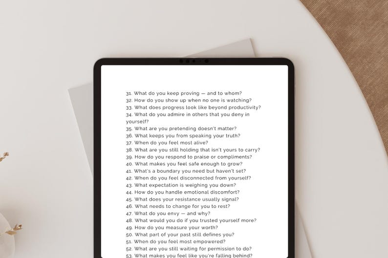 May include: A black tablet displays a list of self-reflection questions in a white font. The questions are numbered and cover topics like self-worth, boundaries, and emotional well-being. The tablet is on a white surface.
