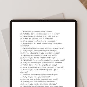 Peut inclure: Une tablette noire affiche une liste de questions d'auto-r&eacute;flexion en texte blanc. Les questions sont num&eacute;rot&eacute;es et couvrent des sujets tels que le stress, les sentiments et les relations. La tablette est sur une surface blanche.