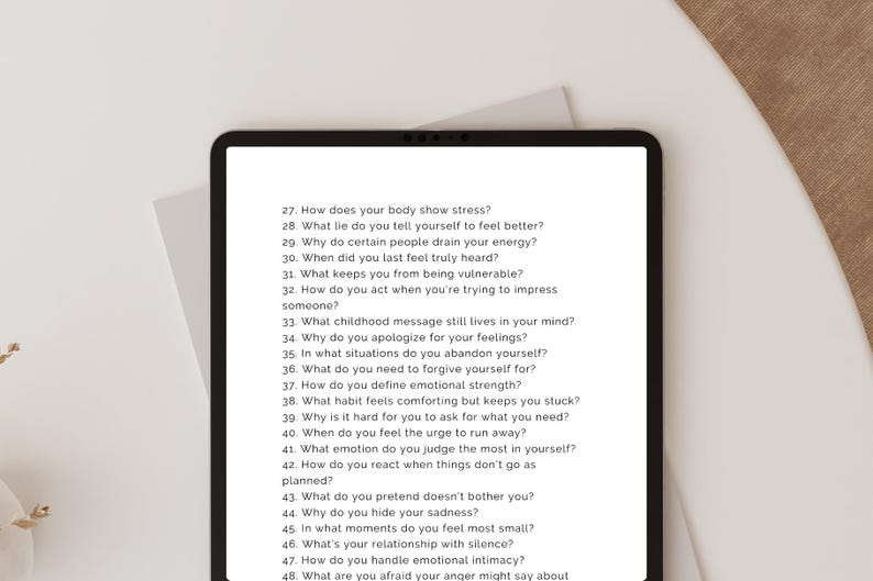 Peut inclure: Une tablette noire affiche une liste de questions d'auto-r&eacute;flexion en texte blanc. Les questions sont num&eacute;rot&eacute;es et couvrent des sujets tels que le stress, les sentiments et les relations. La tablette est sur une surface blanche.