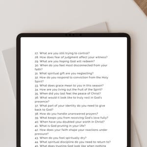 May include: A black tablet displays a list of questions about faith and spirituality. The questions are numbered and written in black text on a white background. The tablet is on a white surface with a neutral background.