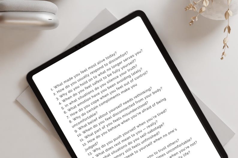 Peut inclure: Une tablette noire affichant une liste de questions d'auto-r&eacute;flexion. Les questions sont en police sans-serif et sont centr&eacute;es sur l'&eacute;cran. La tablette est sur une surface blanche, avec un casque blanc et une plante d&eacute;corative en arri&egrave;re-plan.