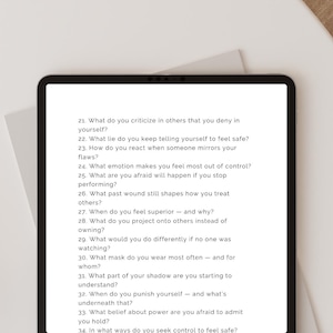 May include: A black tablet shows a list of self-reflection questions in white text. The questions, numbered, focus on personal growth and self-awareness. The tablet is on a white surface.