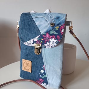 Puede incluir: Bolso bandolera de mezclilla con solapa floral. El bolso presenta un diseño patchwork con varios tonos de mezclilla azul y un acento de tela floral. Tiene una correa de cuero marrón y un cierre de metal. Se ve un pequeño parche de cuero con un logotipo.