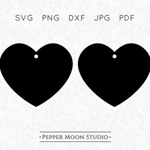 Op de afbeelding: Twee zwarte hartvormige uitsparingen met kleine gaatjes aan de bovenkant om op te hangen. De afbeelding bevat bovenaan de tekst "SVG PNG DXF JPG PDF" en onderaan "PEPPER MOON STUDIO".