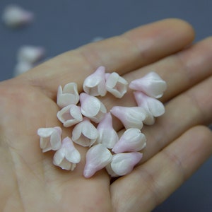 May include: A collection of small, white and pink flower-shaped embellishments. The embellishments are made of a soft, delicate material and have a slightly iridescent finish.