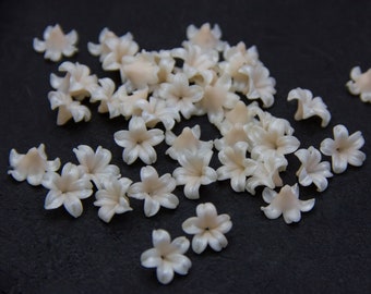 Pode incluir: Uma coleção de pequenas flores de plástico brancas com um leve tom rosado. As flores estão espalhadas sobre uma superfície preta.