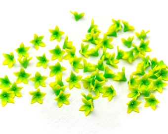 May include: A collection of small, artificial flowers with a star-like shape. The petals are a vibrant yellow, transitioning to a bright green at the tips. These decorative flowers are scattered on a white surface, perfect for craft projects or embellishments.