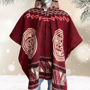 May include: A burgundy poncho with geometric patterns in white, gray, and red. The poncho features a hood and a button closure at the neck. The design includes two large circular motifs and rectangular patterns along the bottom.