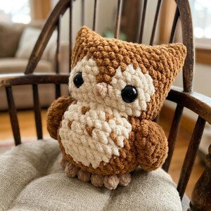 May include: A handmade crochet owl plushie in brown, cream, and beige. The owl has large black eyes and is sitting on a wooden chair with a beige cushion. The owl's body is made of soft, textured yarn.