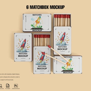 May include: Six matchbox mockups featuring a rocket ship design and the text "Matches Mockup". The matchboxes are white with red and blue accents. The matchboxes are arranged in a grid pattern on a light brown background.