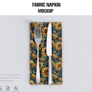 May include: A mockup of a fabric napkin with a sunflower pattern. A silver fork and knife are placed on top of the napkin.