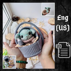 May include: A crocheted doll of a character from a popular science fiction franchise, nestled in a gray basket with a handle. The doll has large black eyes, green skin, and is wearing a pink and beige outfit. A small bottle is also in the basket.