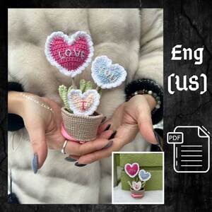 May include: Crocheted flower pot with three hearts that say "Love", "You", and "I". The pot is brown and white and the hearts are pink, blue, and white.