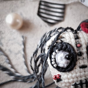 Close-up of the skeleton doll's head, showing its detailed crochet stitching, large black eye, and red accents.