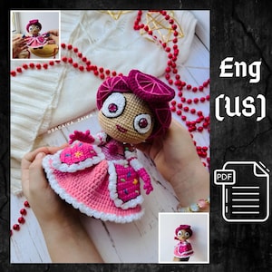 May include: A handmade crochet doll with a pink dress, a matching hat, and large, expressive eyes. The doll has a tan face and a smiling expression. The dress is detailed with white trim and colorful accents. The doll is held in someone's hands.