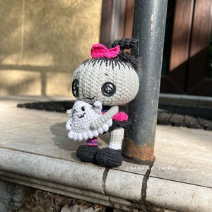 A unique perspective of the doll being held in hand with a blurred city background. The carefully crafted details make this crochet doll pattern an adorable and spooky Halloween gift.
