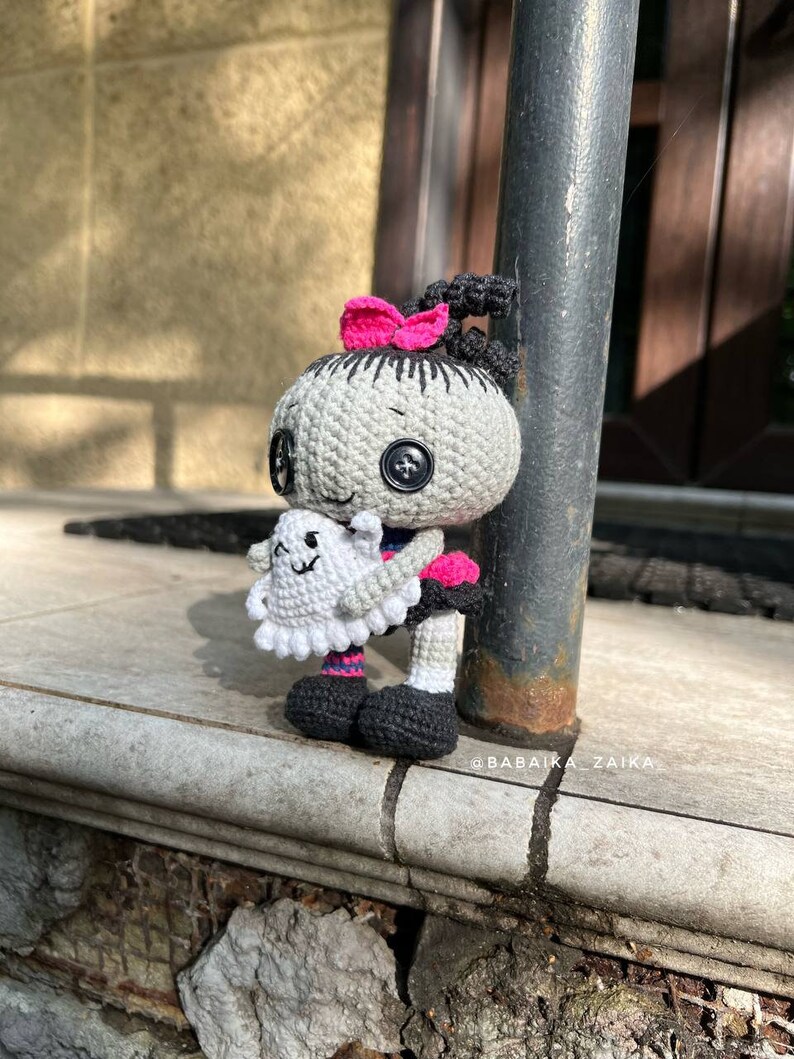 A unique perspective of the doll being held in hand with a blurred city background. The carefully crafted details make this crochet doll pattern an adorable and spooky Halloween gift.
