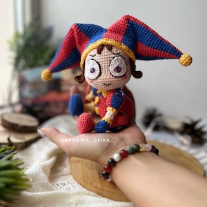 Side angle view of Pomni crochet clown amigurumi, featuring vibrant color tones and a spooky, fun design. Perfect for enhancing Halloween party decor or gifting to handmade toy lovers.