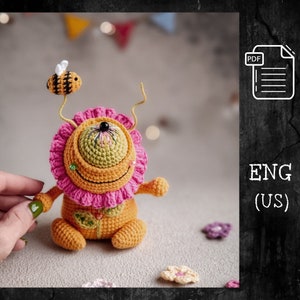 Könnte beinhalten: Häkelanleitung für ein niedliches, farbenfrohes Amigurumi-Monster mit einem großen Auge, einem rosa Rüschenkragen und einer Biene oben drauf. Die Anleitung ist in Englisch (US) verfügbar.