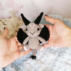 Hand holding the crochet Baphomet amigurumi, focusing on the textured yarn and detailed face of the handmade toy.