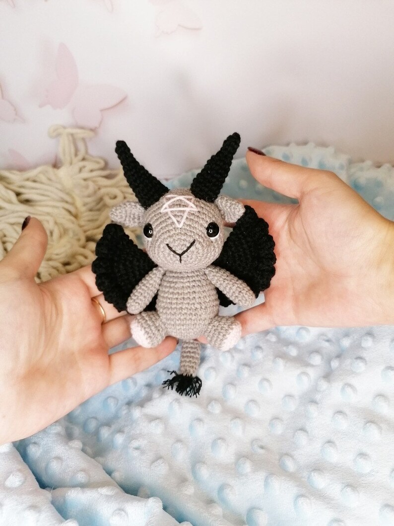 Hand holding the crochet Baphomet amigurumi, focusing on the textured yarn and detailed face of the handmade toy.