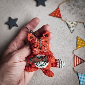 A small crochet cat amigurumi with a fish in its paws, lying on a fabric background. This step-by-step pattern is ideal for craft lovers looking for a handmade crochet project.