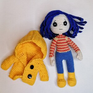 A display of the Coraline doll with her signature blue yarn hair, yellow coat, and detailed accessories, perfect for Halloween or collectible handmade decor.
