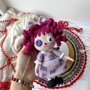 Hand gently adjusting the doll's position, highlighting the dress details and the doll's flexible design.