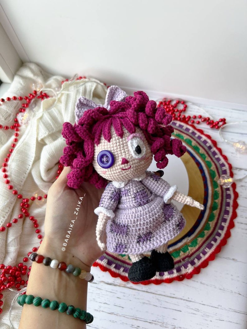 Hand gently adjusting the doll's position, highlighting the dress details and the doll's flexible design.