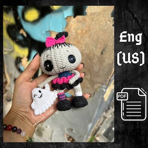 A handmade crochet Halloween doll with a small ghost in its hands, featuring a spooky yet cute design. The doll has a black and gray outfit with pink details, black boots, and a skull-like head. A perfect Halloween amigurumi decoration or gift for crochet lovers.