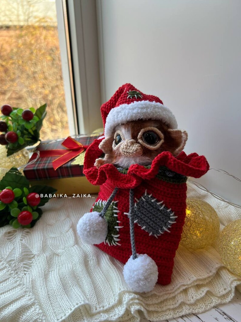 Christmas Gizmo amigurumi in Santa hat, placed among festive holiday decorations, handmade and eco-friendly gift idea.