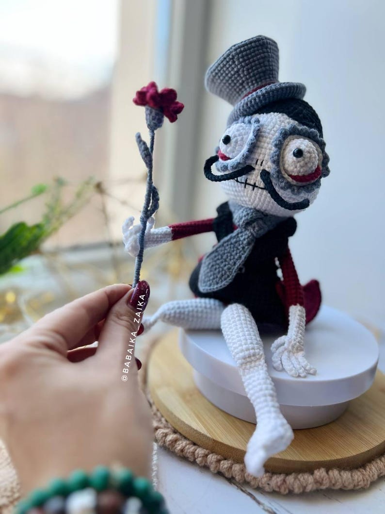 Crochet Mr. Santa Muerte in gray and black colors, holding a red flower, ideal for gothic or Halloween-inspired displays.