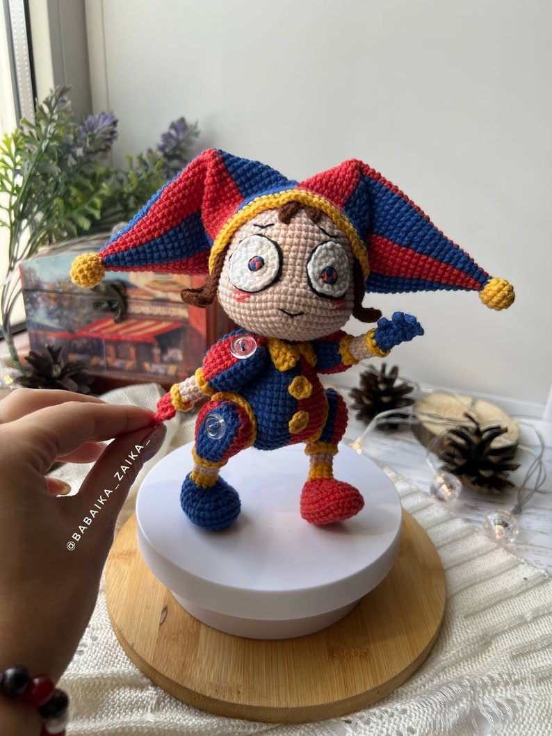 Pomni amigurumi crochet clown doll with a colorful and detailed design, featuring a vibrant jester hat and multi-colored limbs. A great handmade toy for Halloween decor or circus fans.