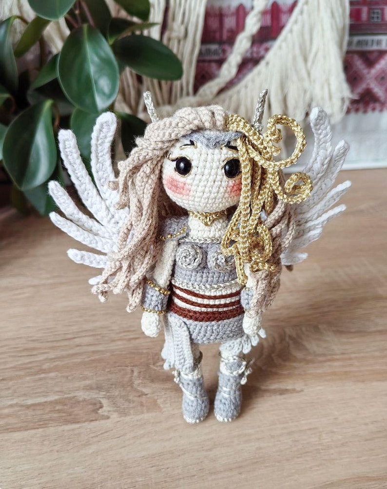 Crocheted valkyrie doll in white wings and armor, standing on wooden table