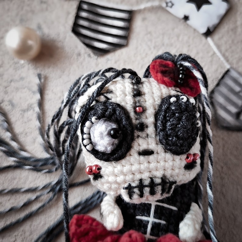 Crochet skeleton doll with long grey yarn hair, posed next to Halloween-themed decorations.