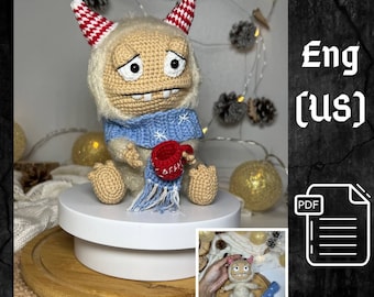 Puede incluir: Patrón de amigurumi de crochet para un lindo monstruo blanco con cuernos rojos y blancos, que lleva una bufanda azul con copos de nieve y sostiene una taza roja. El patrón está disponible en inglés (EE. UU.) y en formato PDF.