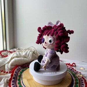 The doll displayed near a window, with natural light highlighting the crochet textures and colors.