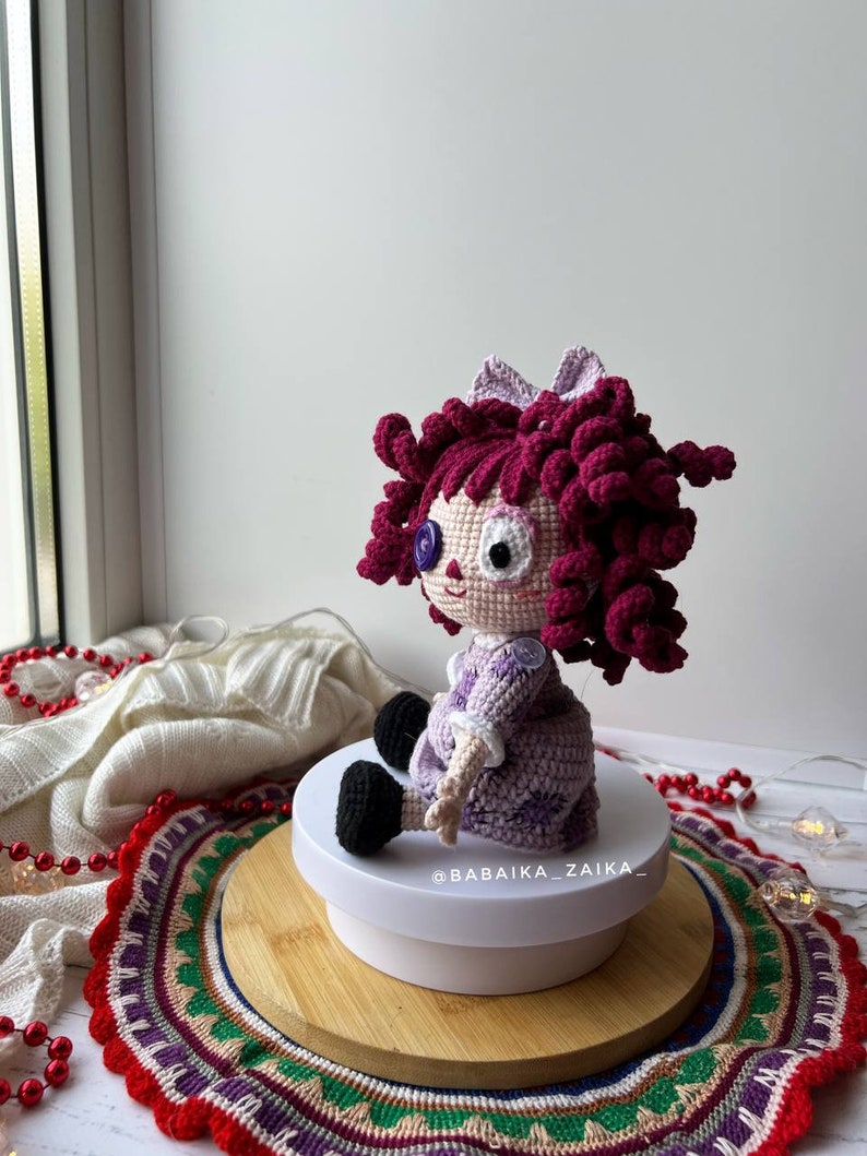 The doll displayed near a window, with natural light highlighting the crochet textures and colors.