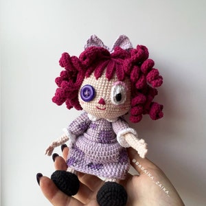 Close-up of the crochet doll with visible hand details, showing the intricate texture of the lavender dress and hair curls.