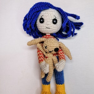 The Coraline doll with its removable raincoat placed beside it, showcasing the outfit customization feature of the crochet pattern.