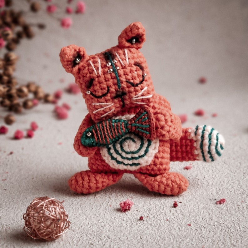 Handmade crochet cat with a tiny fish, designed with eco-friendly materials. This digital amigurumi pattern makes a great DIY craft project for a unique gift.