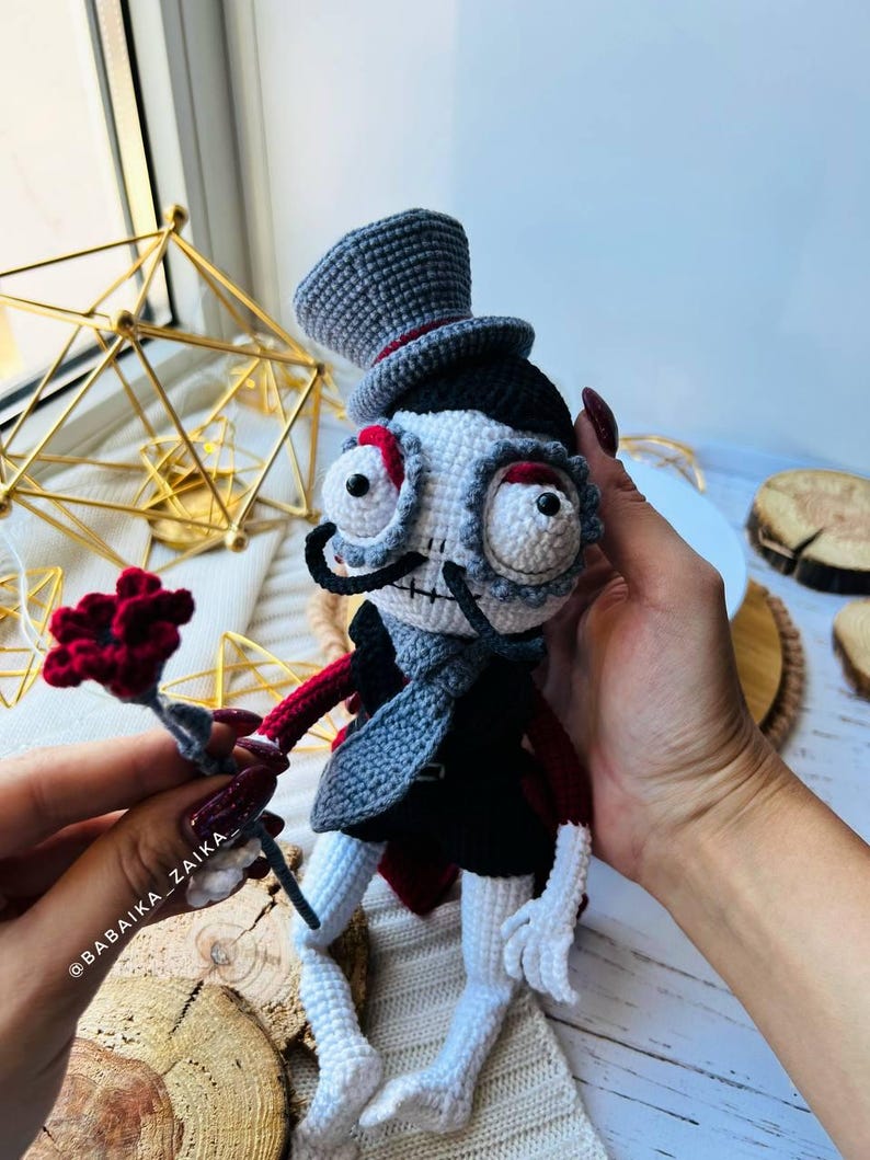 Handmade crochet skeleton doll in black and gray attire, sitting on a wooden display stand with nature-inspired decor.