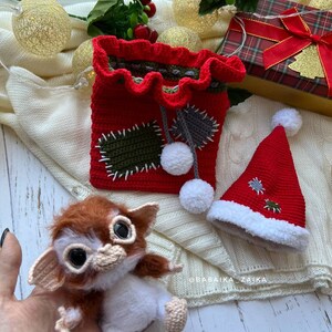 Unique handmade Gizmo amigurumi toy with Christmas bag, perfect for kids, collectors, and festive decor.
Gizmo toy wearing a Santa hat, sitting next to a handmade crochet Christmas bag, eco-friendly and collectible gift idea.