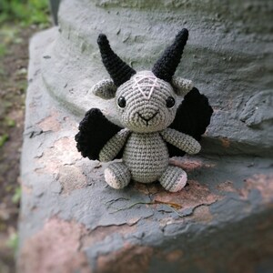Crochet Baphomet toy sitting on a natural stone surface outdoors, blending mystical and natural elements.