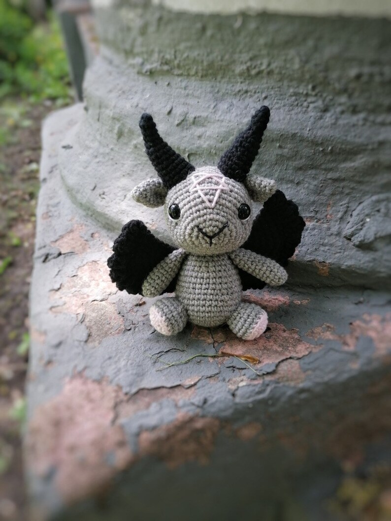 Crochet Baphomet toy sitting on a natural stone surface outdoors, blending mystical and natural elements.