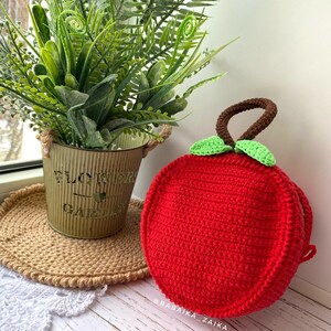 Closed apple-shaped crochet bag displayed with plants, representing a unique and sustainable DIY crafting idea.