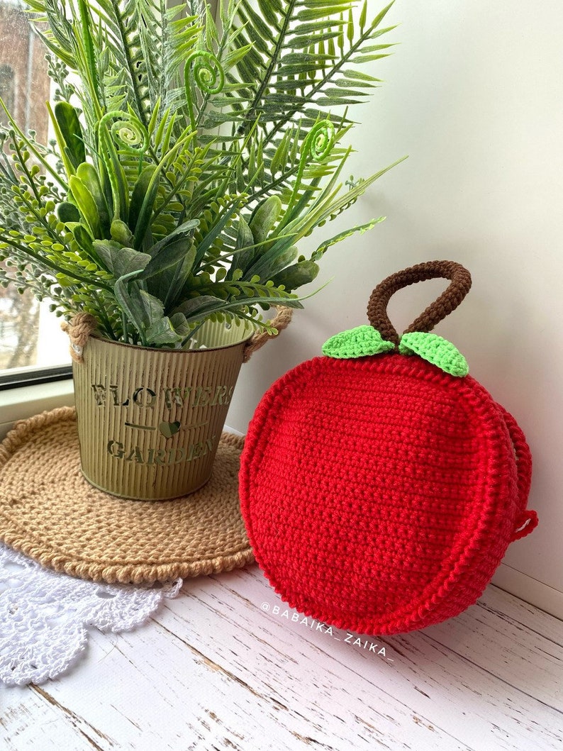 Closed apple-shaped crochet bag displayed with plants, representing a unique and sustainable DIY crafting idea.