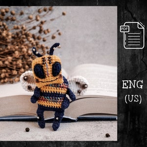 May include: Crochet amigurumi bee toy pattern in PDF format. The bee is yellow and black with blue accents and has a friendly face. The pattern is written in English (US).