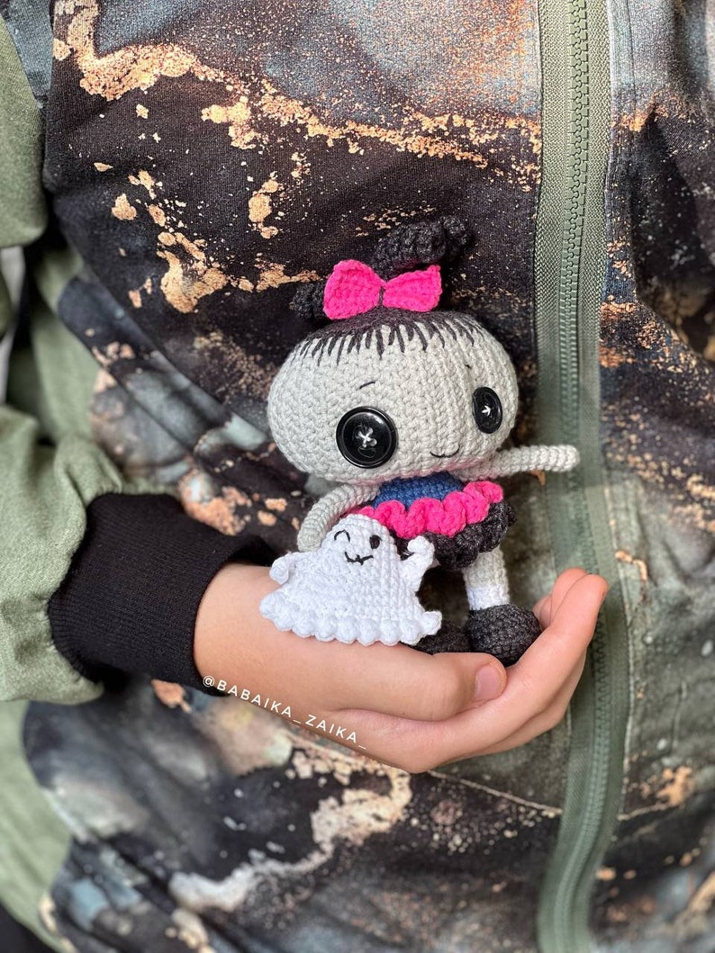 A close-up shot of the doll being held, highlighting its expressive face and fine crochet details. This amigurumi pattern is perfect for those who love Halloween crafts and unique handmade gifts.